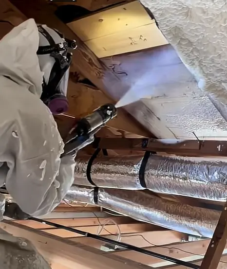 Installer spraying foam around attic rafters and nearby ductwork