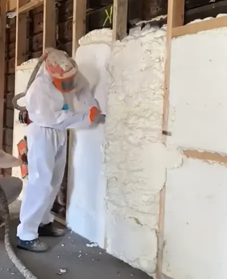 Installer trimming cured spray foam flush with wall framing