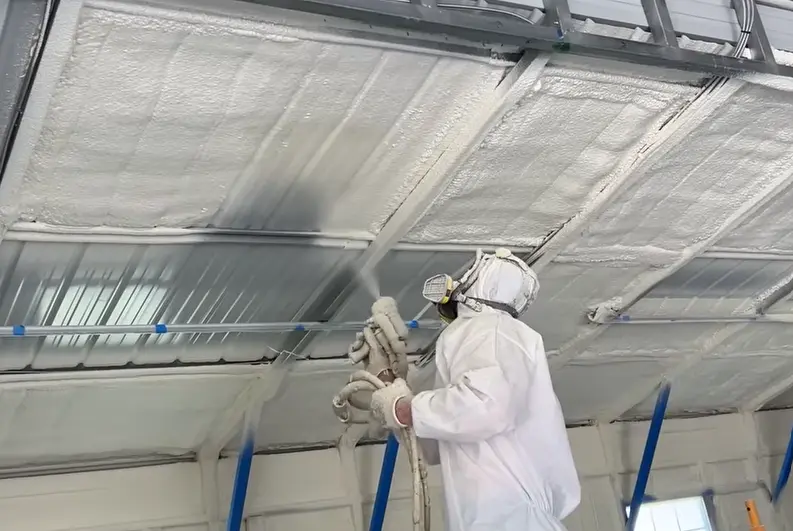 Installer spraying foam beneath a metal garage roof