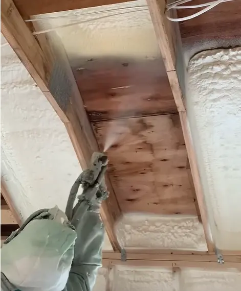 Installer applying spray foam to the underside of a wood subfloor